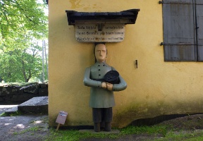 "Vaivaisukko" at the gate of the church. These kinds of usually wooden statues of injured war veterans were common at churches and were used for collecting donations for the assistance of the poor. The text above the figure is from Proverbs 19:17.